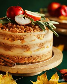 there is a cake with apples on top and leaves around the edges, sitting on a wooden platter