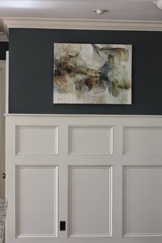 a painting hanging on the side of a wall above a white door with black trim