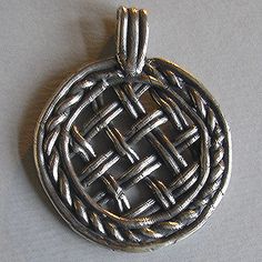 a silver pendant with an intricate design on the front and back side, sitting on a white surface