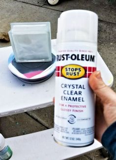 a person holding up a spray paint on top of a white table next to an empty container