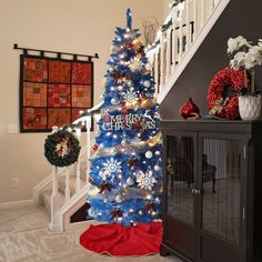 a blue christmas tree with snowflakes and wreaths on it in front of a staircase