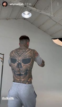 a man with tattoos on his back standing in front of a white wall and light