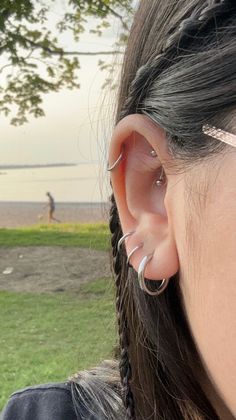 a woman with ear piercings on her ears looking at the water and people in the distance