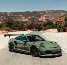 a green sports car parked on the side of a road with mountains in the background