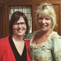 two women standing next to each other in front of wooden cupboards, smiling for the camera