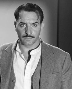 a man with a moustache wearing a suit and tie looking at the camera