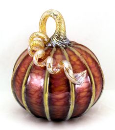 a red and gold glass pumpkin ornament sitting on a white surface with two twisted handles