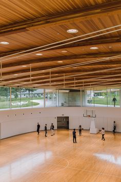 people are playing basketball in an indoor gym with wood floors and large windows on the ceiling