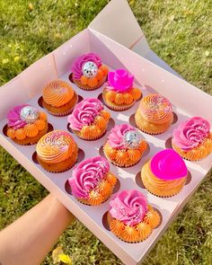 a box filled with lots of cupcakes on top of a grass covered field