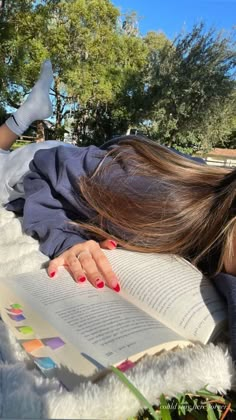 a woman laying down reading a book in the grass with her head on top of an open book