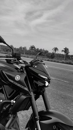 a black and white photo of a motorcycle parked on the side of the road with palm trees in the background