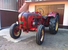 an old red tractor is parked in front of a garage with stairs and a door