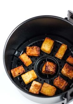 tofu cubes cooking in an air fryer on a white table top,