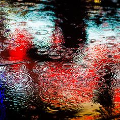 rain drops on the ground with red, white and blue lights reflected in it's surface