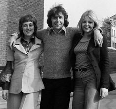 three women standing next to each other in front of a brick building with one woman holding her arm around the other