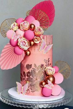 a pink cake with gold decorations and flowers on the top is sitting on a platter