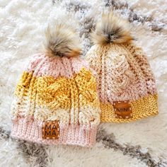 two knitted hats with fur pom poms on top of a white rug