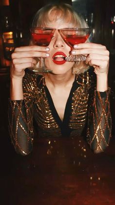 a woman with red lipstick holding up two glasses to her face while sitting at a table