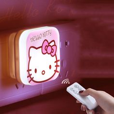 a person holding a remote control in front of a hello kitty light