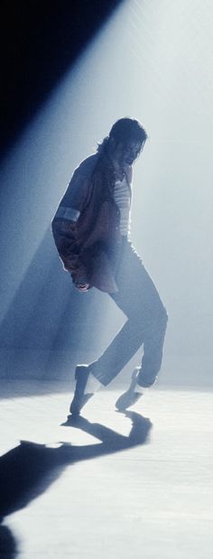 a man is dancing in the middle of a dark room with light coming from behind him