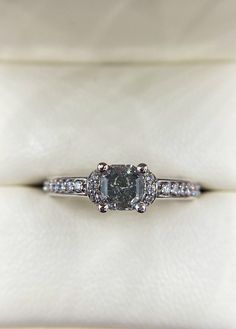 A Fancy Gray radiant cut diamond engagement ring set in 14k white gold. It has a total carat weight of 1.00 TCW. The center stone is a Fancy Gray diamond with a carat weight of .60 and a clarity of SI2. The colorless side diamonds go 3/4 of the way down on the shank, are F-G in color, VS1-VS2 in clarity, with a carat weight of .40. Featuring a recessed halo, this cool-toned gray engagement is a good choice for a true silver look.  A matching wedding band is available for this ring. Please contact us for matching bands as prices may vary depending on the current market price of precious metals The ring is set in a standard size 7 but can be resized two sizes up or down. If you will need a size larger or smaller than this, it will need to be made in your size. Please contact us for us for cu Gray Engagement Ring, Radiant Diamond Engagement Ring, Radiant Diamond Engagement Rings, Radiant Cut Diamond Engagement Rings, Gray Diamond, Market Price, Radiant Cut Diamond, Diamond Engagement Ring Set, Radiant Diamond