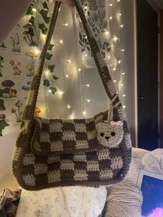 a crocheted cat purse hanging from a wall with christmas lights in the background