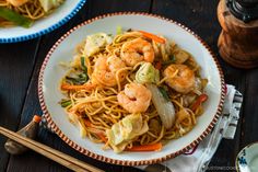 two plates filled with noodles and shrimp on top of a table next to chopsticks