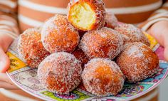 powdered sugar coated donuts on a plate being held by a woman's hands