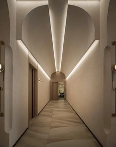 an empty hallway with white walls and lights on either side of the corridor, leading to another room