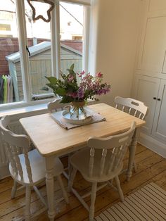 a wooden table with white chairs and a vase filled with flowers on top of it