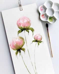 a watercolor painting of three pink flowers next to some paintbrushes on a white surface