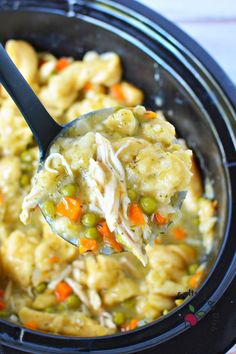 a spoon full of chicken noodle soup in a crock pot with carrots and peas