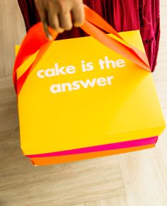 a person holding a yellow box that says cake is the answer