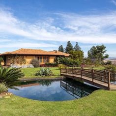 a wooden bridge over a small pond in front of a house with a large garden