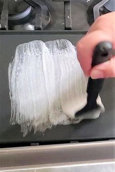 a person is using a brush to paint the side of a stove with white paint