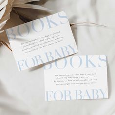 two books for baby are laying on a bed with white sheets and paper flowers in the background