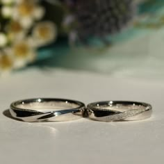 two wedding rings sitting next to each other on a white surface with flowers in the background