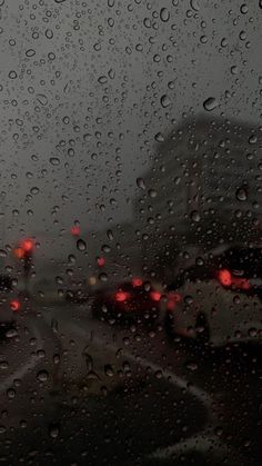 rain drops on the windshield of a car as it drives down a street with red traffic lights