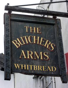 the butcher's arms whitbread sign is hanging from the side of a building