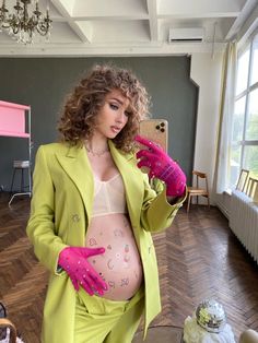 a woman in a green suit and pink gloves taking a selfie with her cell phone