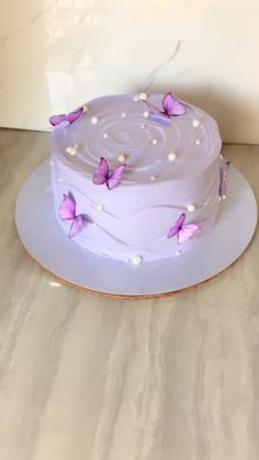 a purple cake with pink butterflies on it sitting on a white plate next to a wall