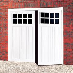 two white garage doors with black trim on the side of a red brick building,