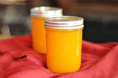 two jars filled with orange liquid sitting on top of a red cloth