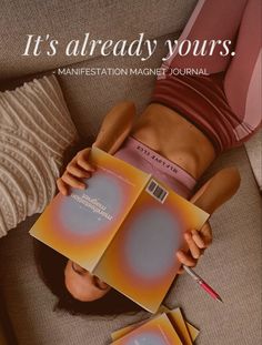 a woman laying on top of a couch holding two magazine's in her hands