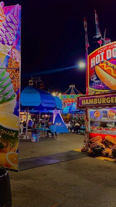 an amusement park with many rides and food stalls at night, including hotdog stand