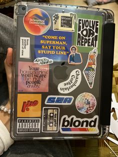 a person holding an apple laptop covered in stickers and decals on its cover