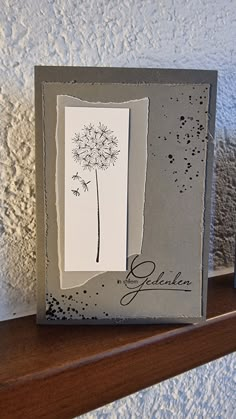 a card with a dandelion on it sitting on top of a wooden shelf