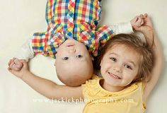 two young children laying next to each other on top of a white floor with one holding the head of another child