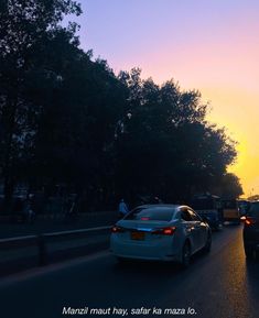 cars driving down the road at sunset with trees in the backgrouund and people walking on the sidewalk