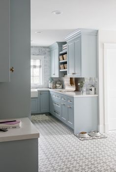 a kitchen with light blue cabinets and white tile flooring, along with an open window